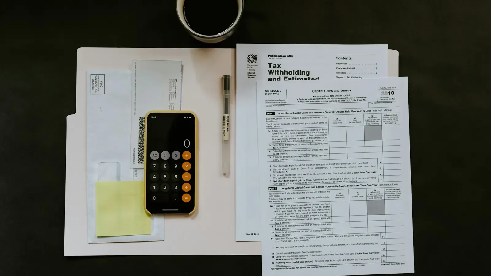 Papéis fiscais, calculadora, celular e uma caneca de café sobre uma mesa de trabalho escura