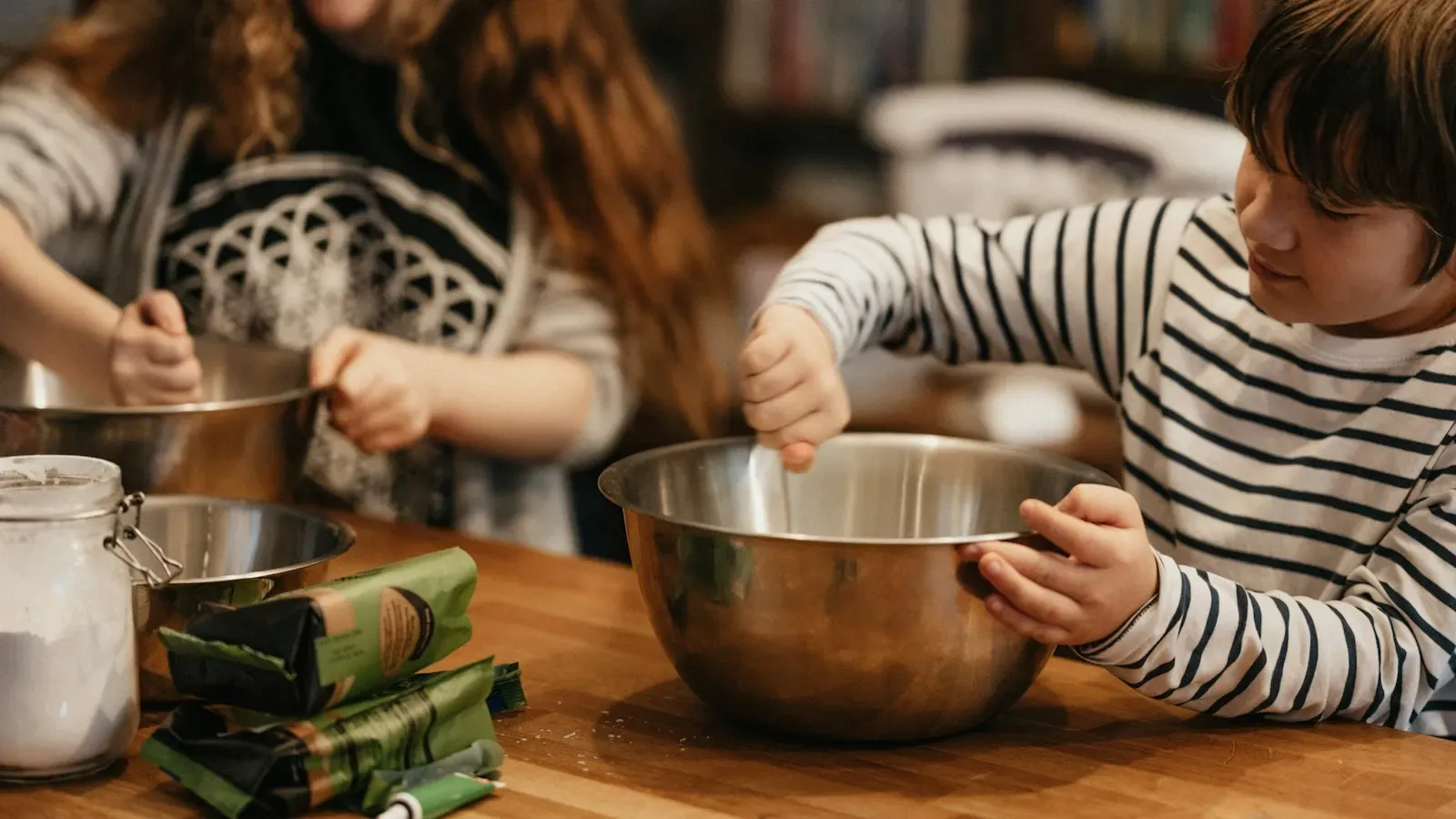 Duas pessoas batendo massa em tigelas de inox na cozinha de casa