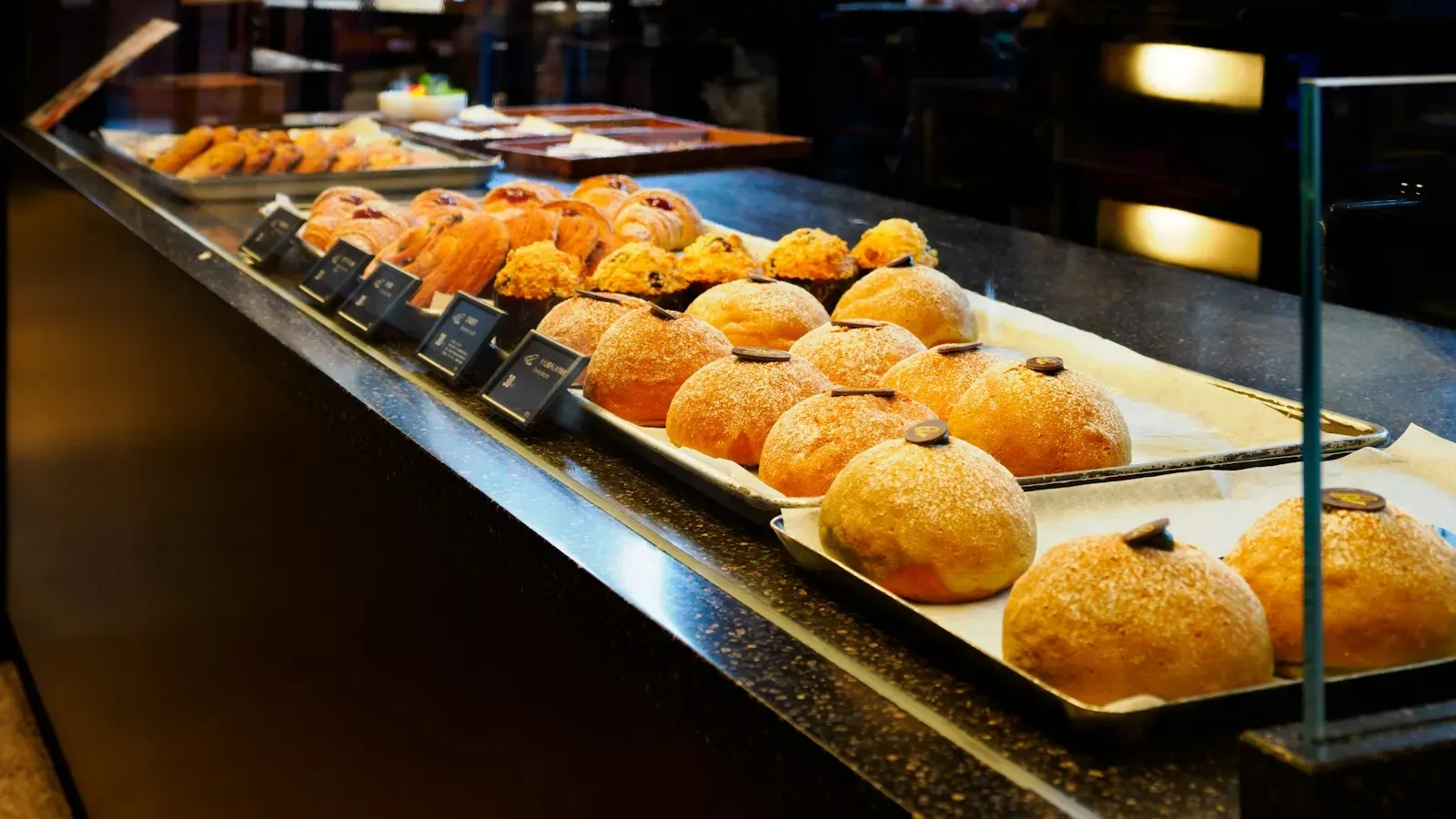 A small bakery counter with trays of buns, each with its own price card